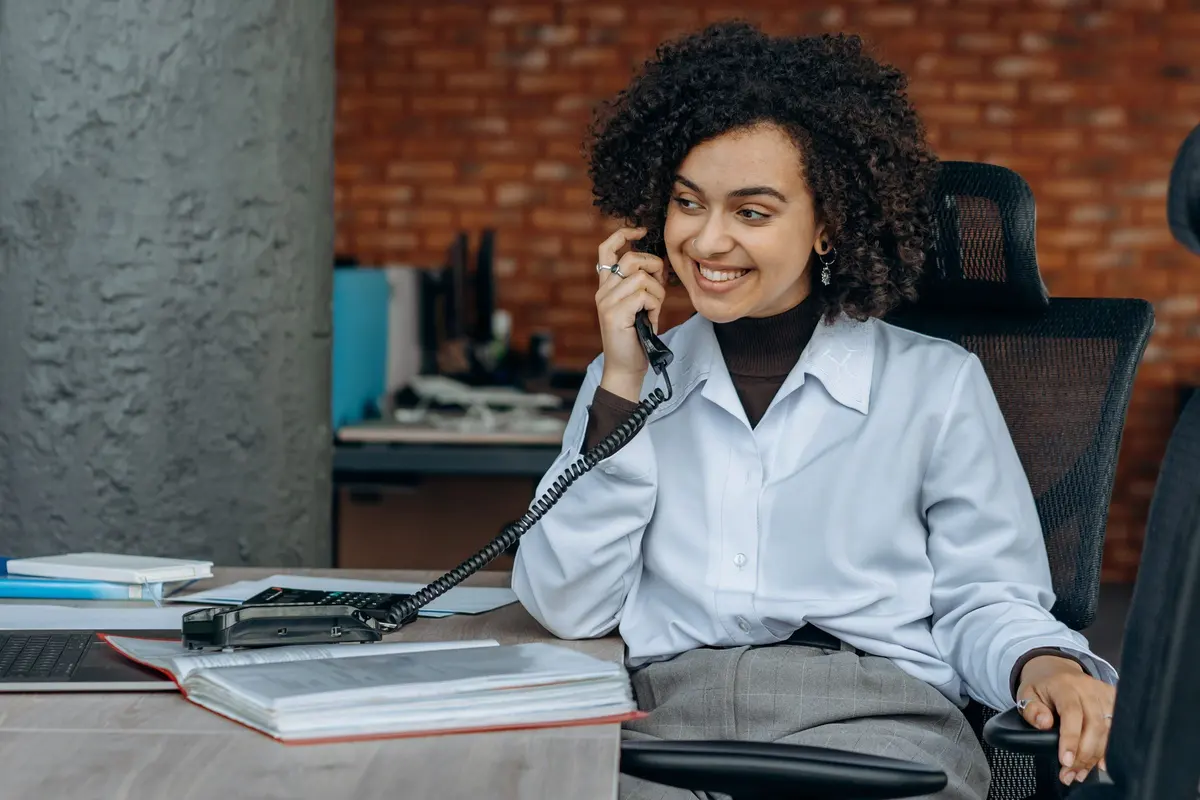 Mulher sorri enquanto atende ao telefone em sua mesa de trabalho
